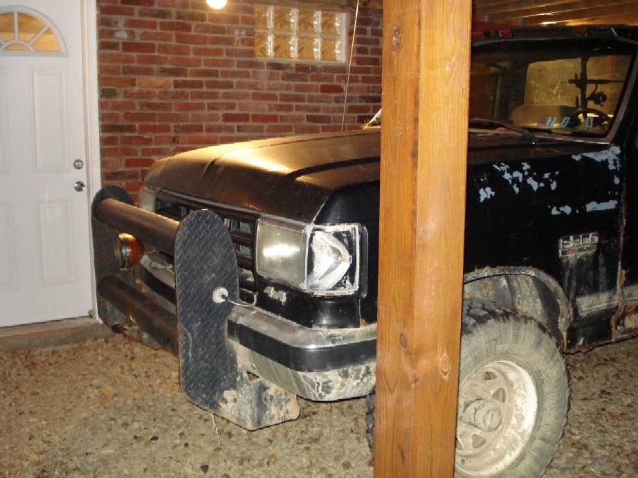 Black Ford F-series truck with a push bumper, parked indoors. The truck is dirty and has some paint damage