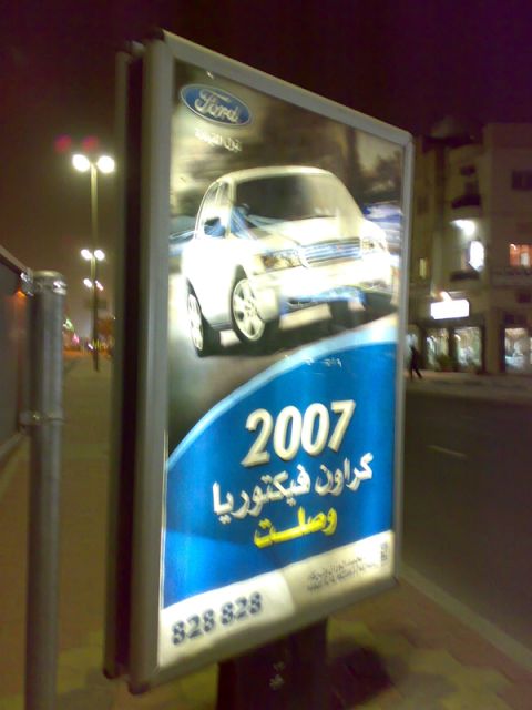 1999 Mercury Grand Marquis - A billboard displays a 2007 Ford vehicle with Arabic text below.