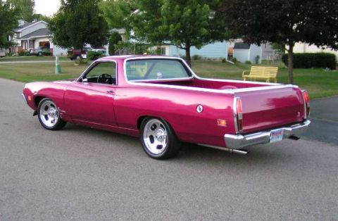 1973 Ford Ranchero - This pink Ford Ranchero is parked on a street in front of houses and trees.