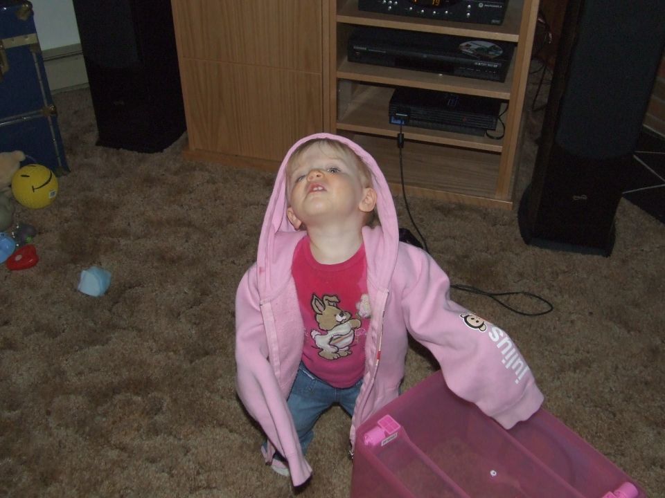 Young child in a pink hoodie kneeling on living room carpet
