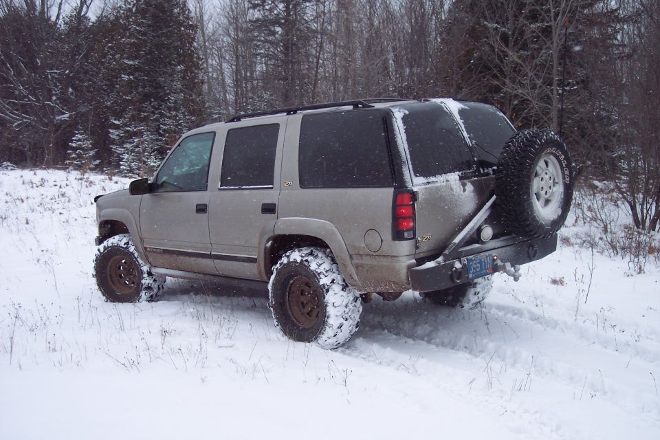 Silver Chevrolet Tahoe with spare tire mounted on rear bumper, driving in snow