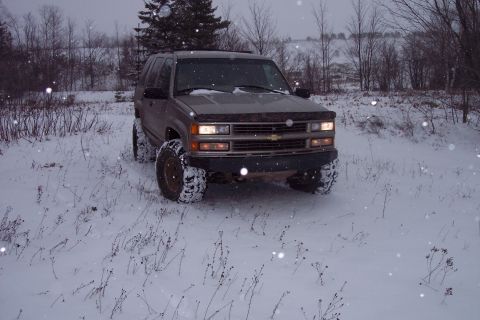 2000 Chevrolet Tahoe - A brown Chevrolet Tahoe with large tires drives through a snowy field.