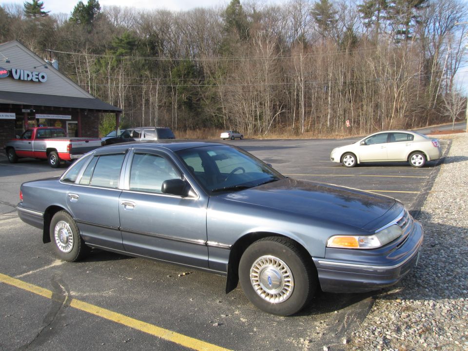 Blue sedan parked in a lot, front quarter view. Visible chrome trim, aftermarket window visors, and distinctive grille