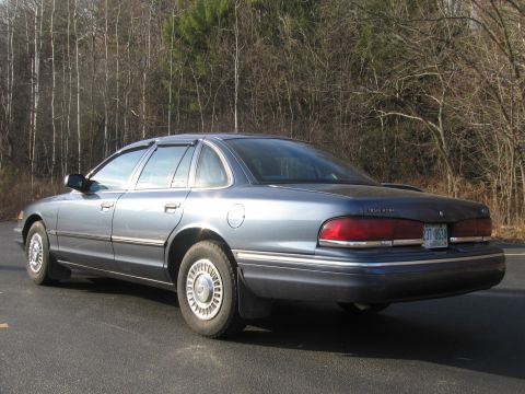 1991 Ford LTD Crown Victoria - The rear of a blue Ford Crown Victoria sedan is shown parked on a road with trees in the background.