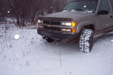 2000 Chevrolet Tahoe - A silver Chevrolet Tahoe with large off-road tires sits in a snowy landscape, its front bumper visible.
