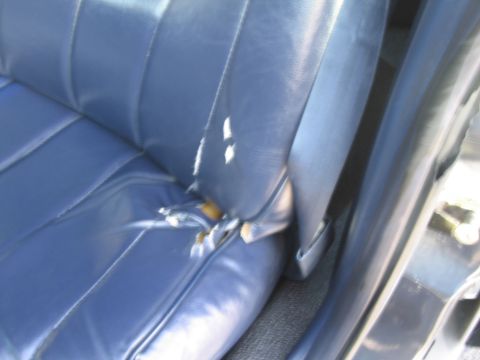 1991 Ford LTD Crown Victoria - The interior of a vehicle shows a worn blue seat with significant tears exposing the underlying foam.