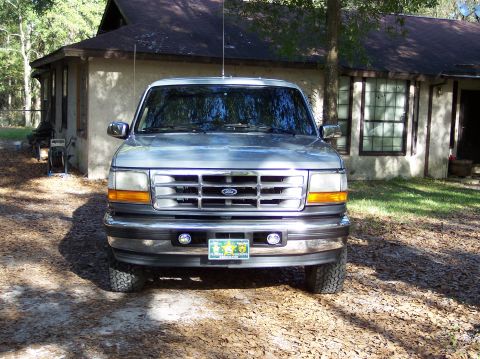 1996 Ford Bronco - A silver 1996 Ford Bronco is parked on a dirt driveway in front of a house.