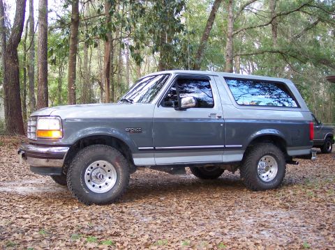 1996 Ford Bronco - Side view of a two-tone grey 1996 Ford Bronco parked outdoors with trees and foliage.