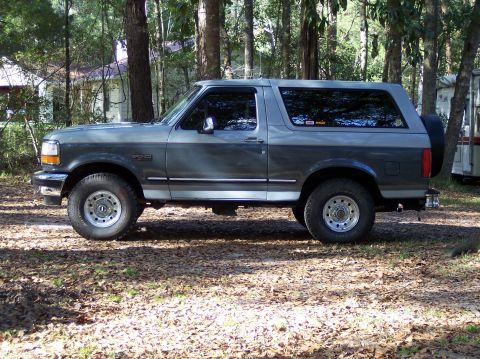 1996 Ford Bronco - This Ford Bronco is parked on a dirt lot surrounded by trees, with a spare tire mounted on the back.