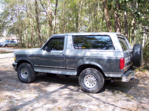 1996 Ford Bronco - A two-tone Ford Bronco is parked outdoors with trees in the background, and another car is visible in the distance.