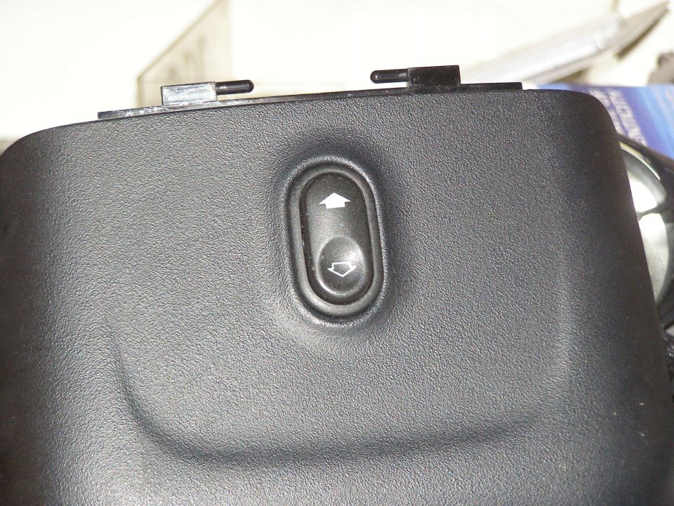 Close-up of a black plastic panel with an oval-shaped power window switch. The switch has up and down arrows