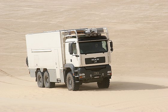 White MAN expedition truck with camper body driving on sand dunes