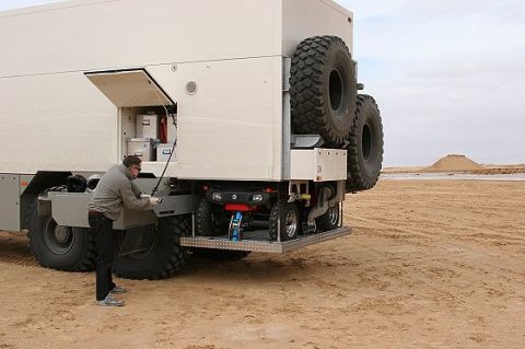 1993 Ford Bronco - A man inspects the rear storage compartment of a large expedition truck, which carries an ATV on a rack.