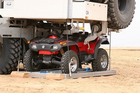 1993 Ford Bronco - A red ATV is positioned on a platform beneath a larger vehicle, with desert terrain in the background.
