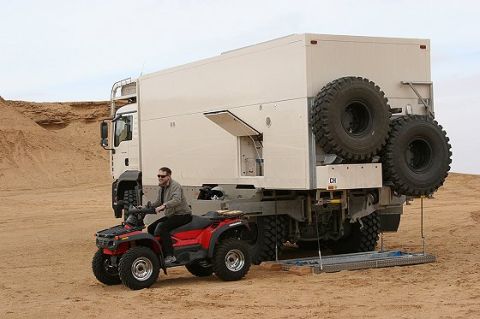 1993 Ford Bronco - An expedition truck is parked in a sandy area, with a man riding an ATV in front of it.