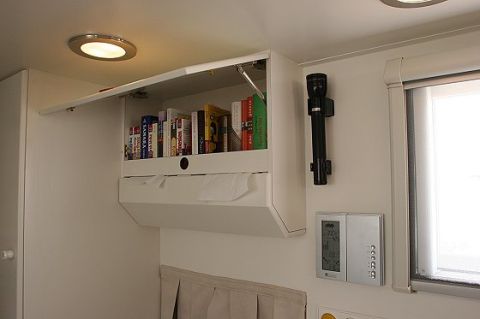 1993 Ford Bronco - Interior view of an RV showing a cabinet filled with books, a flashlight, and a thermostat on the wall.