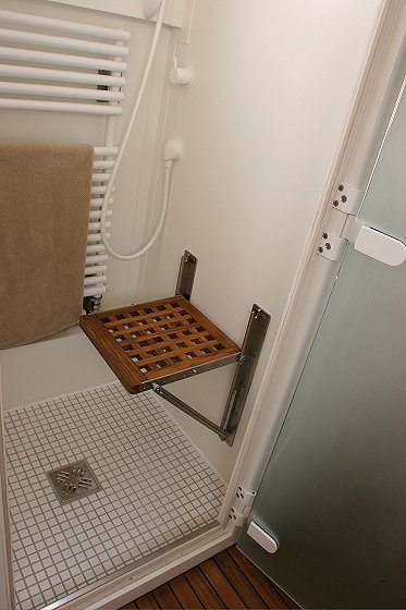 1993 Ford Bronco - A fold-down wooden seat is mounted on the wall of a shower stall with a tiled floor and a towel rack.