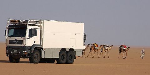 1993 Ford Bronco - A MAN truck with a camper body travels through a desert landscape, accompanied by camels.