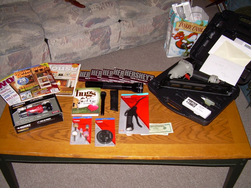 Coffee table with magazines, Hershey's bars, a flashlight, a book, a microphone, a nail gun in a case, and other tools
