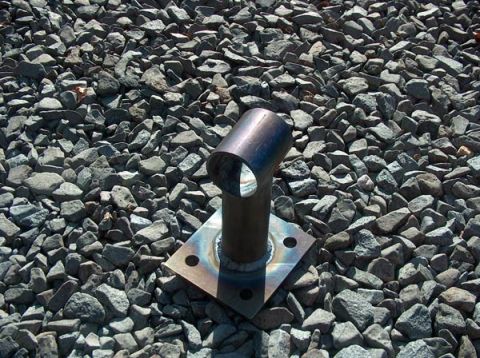 1991 Ford Bronco - A metal pipe fitting is mounted on a square base plate on a gravel surface.