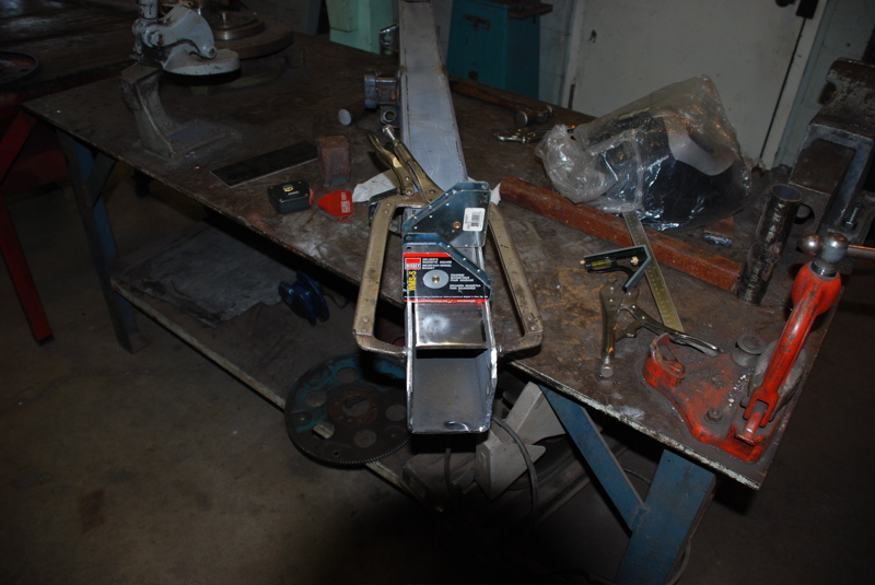Metal bracket held by large clamps on a workbench with tools