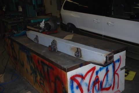 1996 Ford Bronco - A fabricated metal bumper part rests on a workbench covered in graffiti.