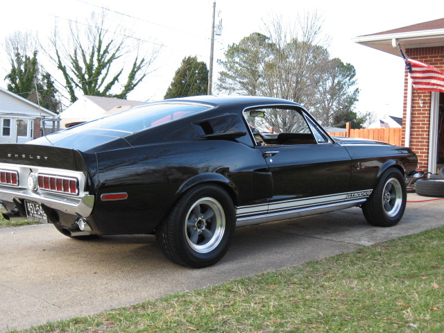 Black 1968 Shelby GT500 parked on driveway, rear quarter view. Shelby and GT500 lettering visible