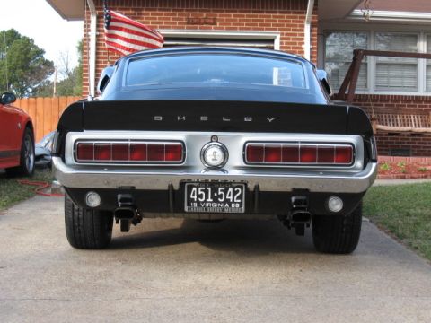 1968 Shelby GT500 - The rear of a black 1968 Shelby GT500 is shown, parked in front of a brick house.