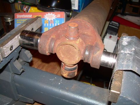 1988 Ford Bronco - A close-up view of a rusty driveshaft U-joint being held in a vise, with a socket wrench attached to one of the yokes.