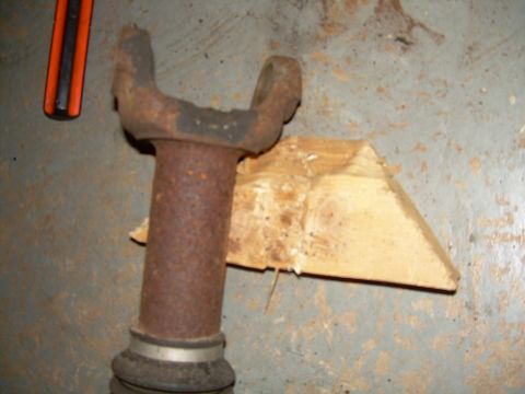 1988 Ford Bronco - A rusty driveshaft U-joint is shown with a wooden wedge and tool fragment of a tool.