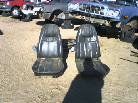 1973 Ford Ranchero - A pair of black bucket seats are shown in a junkyard, with other vehicles visible in the background.