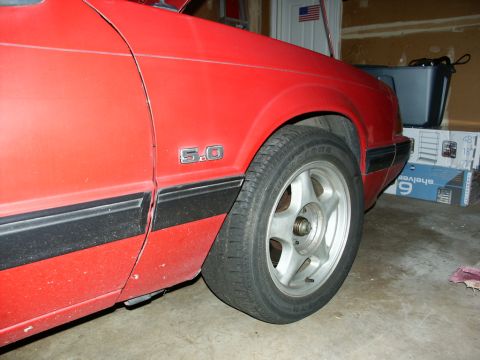 1990 Ford Mustang - Close-up of the side of a red 1990 Ford Mustang, showing the fender and wheel.