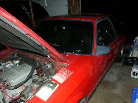 1990 Ford Mustang - A red 1990 Ford Mustang coupe is shown with its hood open, revealing the engine and two manuals on the fender.