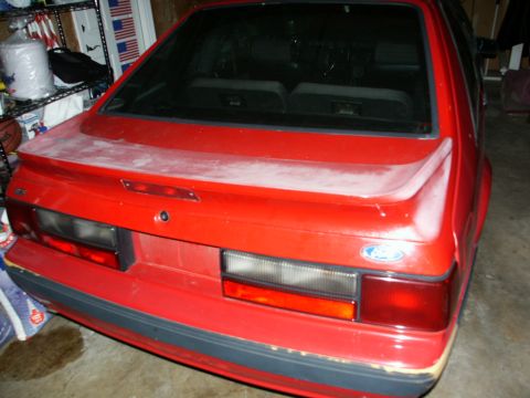 1990 Ford Mustang - The rear of a red 1990 Ford Mustang shows a dusty finish and a prominent spoiler.