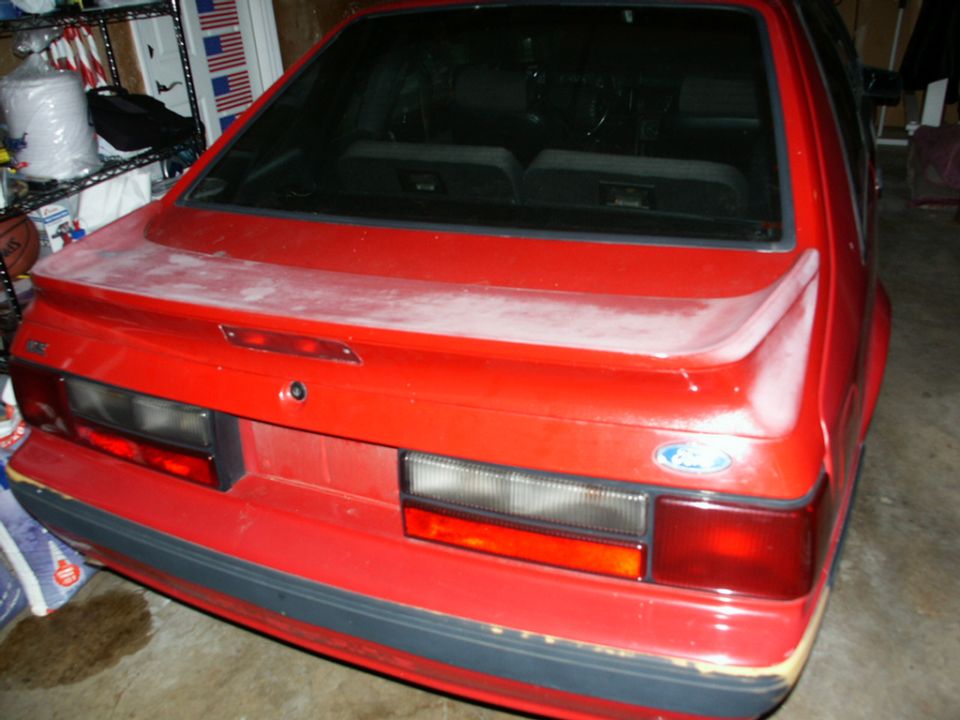 Red 1990 Ford Mustang rear view, dusty finish, with a spoiler and a Ford emblem