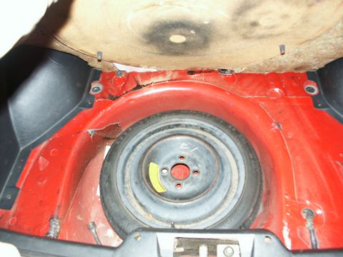 1990 Ford Mustang - Spare tire well in a vehicle, showing the spare tire and surrounding red painted metal.