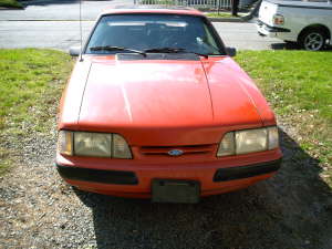 Orange 1990 Ford Mustang front view, showing headlights, grille, and hood