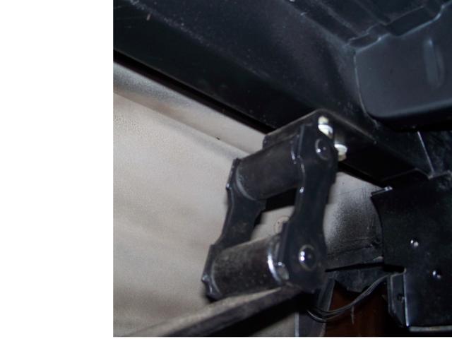 Close-up of a black metal shackle with bushings, part of a vehicle's rear suspension system