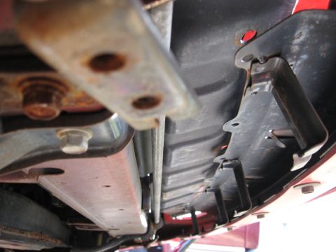 1991 Mitsubishi 3000GT - Close-up view of the undercarriage components of a red vehicle, revealing various metal and plastic parts.