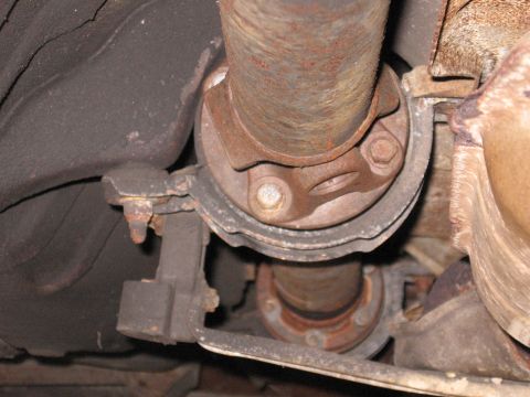 1991 Mitsubishi 3000GT - Underside view of a vehicle's rusty driveshaft and exhaust system components.