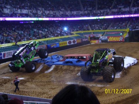 1993 Ford Bronco - Two monster trucks compete in a stadium event, with a crowd watching from the stands.