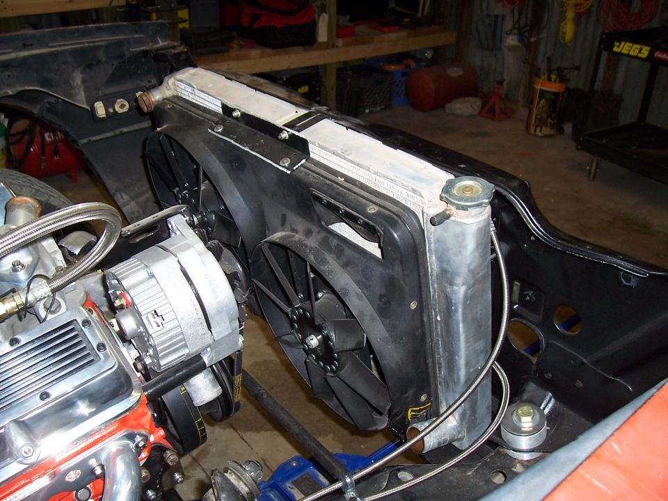 Aluminum radiator with dual electric fans beside orange V8 and alternator in bare engine bay