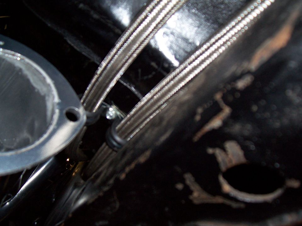 Close-up of braided stainless lines clamped to a black-painted underbody panel
