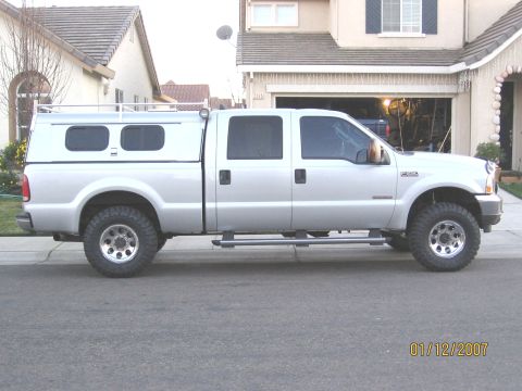 2004 Ford F-250 - Side view of a silver 2004 Ford F-250 Super Duty pickup truck equipped with a camper shell and aftermarket wheels.
