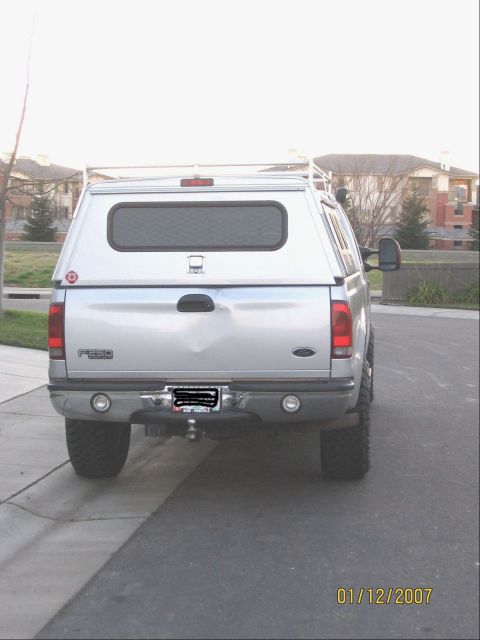 2004 Ford F-250 - Rear view of a silver 2004 Ford F-250 pickup truck equipped with a camper shell and aftermarket wheels.