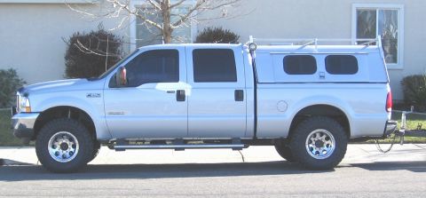 2004 Ford F-250 - Side view of a silver 2004 Ford F-250 pickup truck equipped with a camper shell and roof rack.