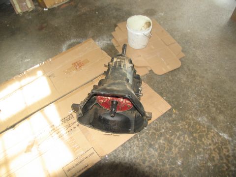 1978 Ford Bronco - A transmission assembly is shown on cardboard, with a white bucket nearby.