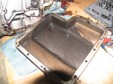 1978 Ford Bronco - A dirty transmission oil pan sits beside a disassembled transmission and a toolbox, indicating a repair or maintenance task.