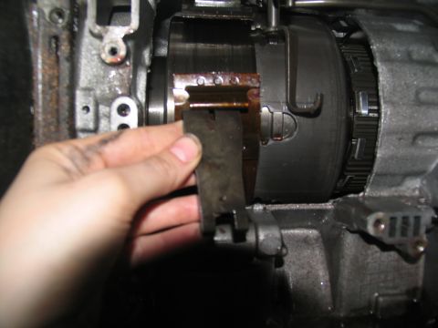 1978 Ford Bronco - Close-up of a hand holding a metal clip within a transmission assembly, likely during a tear-down or repair process.