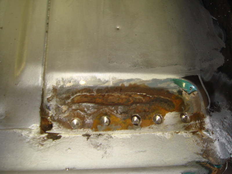 Close-up of rusted metal with rivets, likely part of a vehicle floor repair